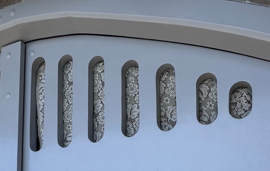 Lace showing through a row of rounded slots in a pale blue metal panel