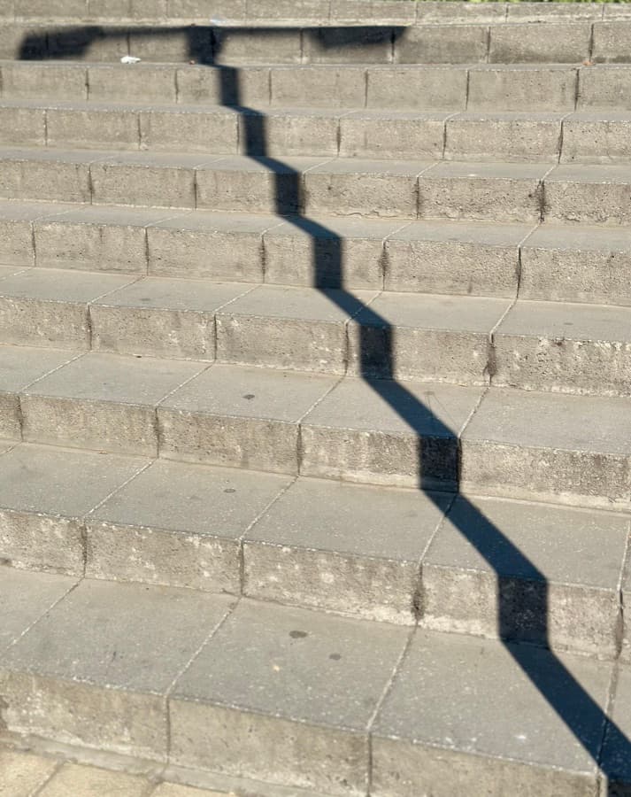 A railing's shadow zigzagging down concrete steps